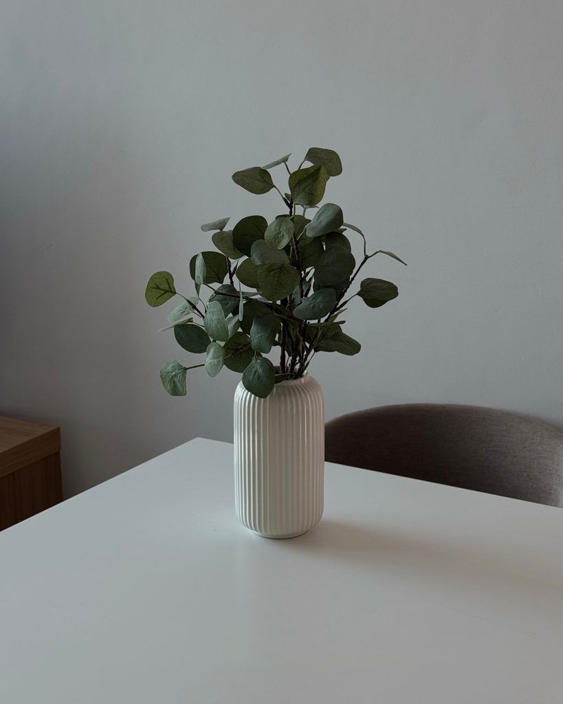 White ribbed ceramic vase filled with green stems on a minimalist dining table.