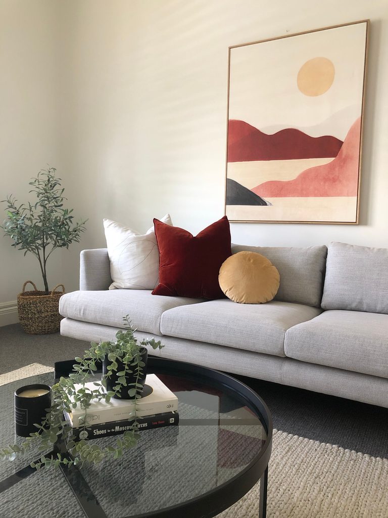 Neutral living room with burgundy and golden throw pillows arranged on a light gray sofa.