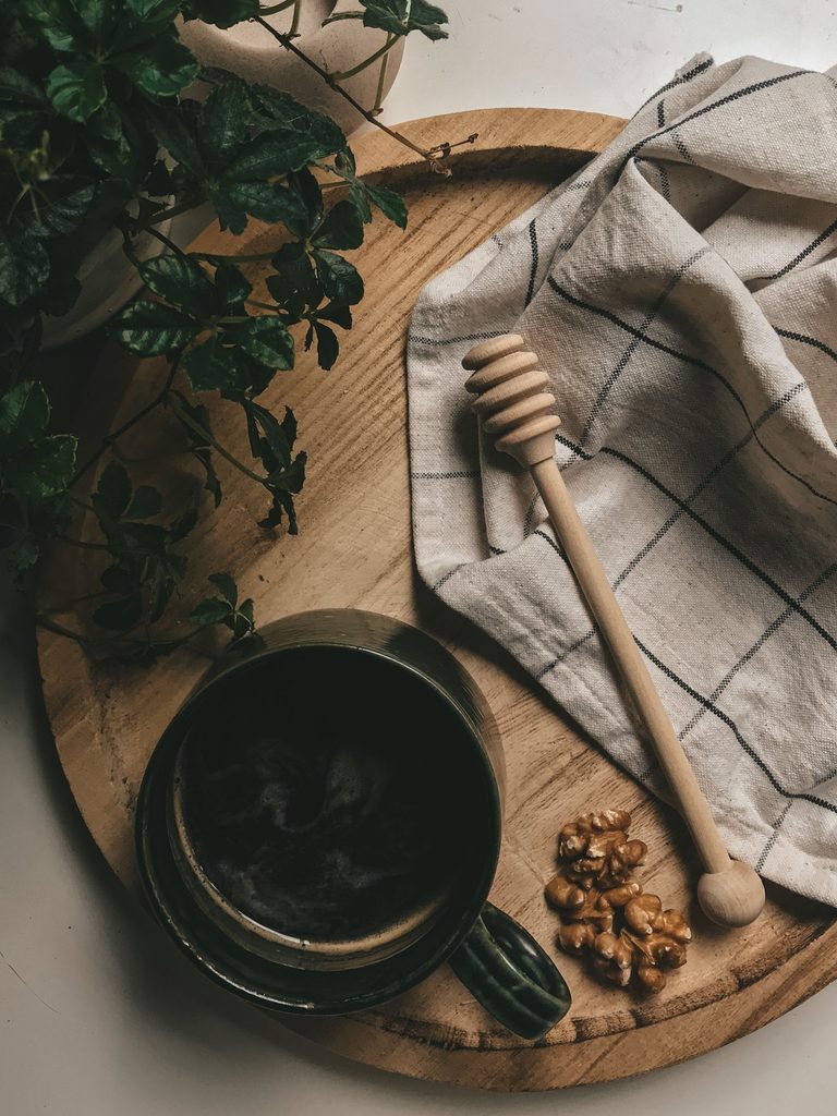 Round wooden tray styled with a dark mug, greenery, linen cloth, and wooden honey dipper.