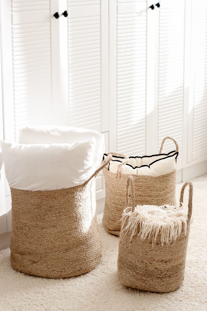 Woven storage baskets filled with pillows and a throw blanket in a bright, cozy room.