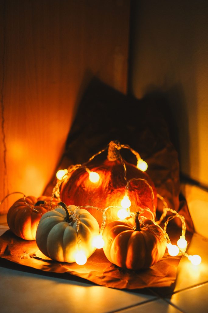 Whimsical Halloween decor with orange and white pumpkins surrounded by glowing string lights.