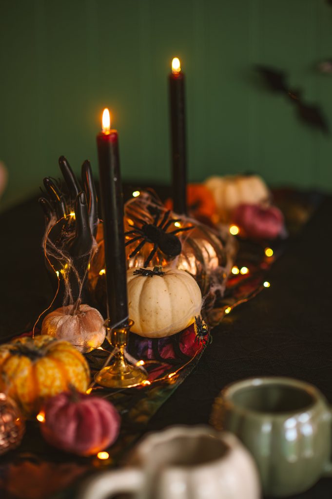 Indoor Halloween decor with pumpkins, black taper candles, spider web decorations and string lights arranged on a table.